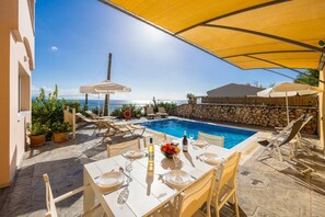A poolside dining area with a table set for two, overlooking a swimming pool and the sea. - Villa Cleo Beach in Mparmpati (Corfu)
