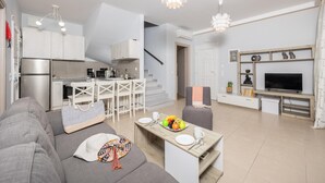 Een modern appartement met een keuken, eethoek en woonkamer. Het heeft een trap, een televisie en een bank.