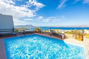 Piscina no terraço com águas azul-claras, rodeada por espreguiçadeiras e plantas em vasos, com vista para o horizonte costeiro.