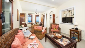 A living room with wicker furniture, a television, and a dining area with a table and chairs. - Villa Ikaros in Plaka (Apokoronas)