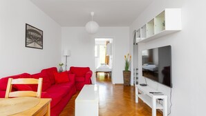 Una sala de estar moderna con un sofá rojo, una mesa de centro blanca, un televisor y un cuadro en la pared.