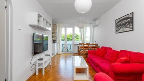 Una sala de estar moderna con un televisor de pantalla plana, un sofá rojo, una mesa de centro blanca y una zona de comedor con una mesa y sillas.