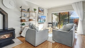 Un salon moderne avec une cheminée, des canapés gris, un téléviseur et une grande fenêtre donnant sur des arbres et des montagnes.