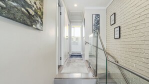 A modern hallway with a glass railing, a white brick wall, and a framed picture on the wall. - Albi Celeste - 2/9 Park Road (Jindabyne)