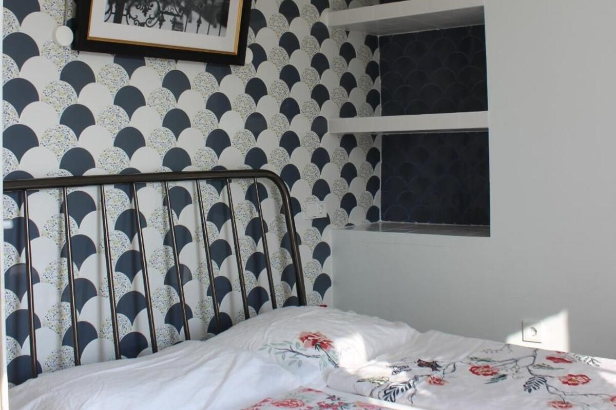 Une chambre à coucher avec un lit, une horloge murale, un tableau encadré et un papier peint à motifs.
