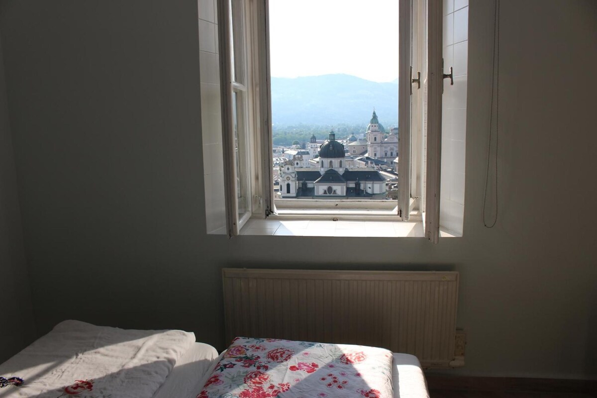A bedroom with a bed, a radiator, and a window with an open shutter.