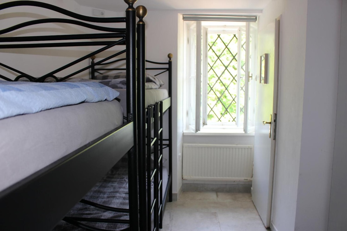 Une chambre avec un lit superposé, une fenêtre ornée d’un motif en treillis et un radiateur.