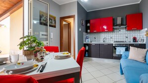 A modern kitchen with red cabinets, a dining area with a table set for two, and a blue sofa in the living area. - Villa Tiffany with Private Terrace, Wi-Fi, Air Conditioning, and Garden View (Campofelice di Roccella)