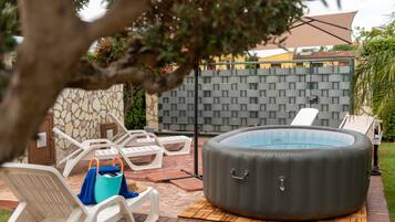 Ein Außenbereich mit Whirlpool, Liegestühlen, einer Steinwand und einer gefliesten Terrasse.
