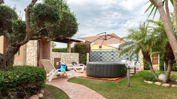 A patio area with lounge chairs, a hot tub, and a stone wall. - Villa Tiffany with Private Terrace, Wi-Fi, Air Conditioning, and Garden View (Campofelice di Roccella)