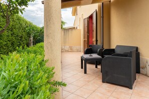 An outdoor patio with wicker furniture, a tiled floor, and a building with a red door in the background. - Villa Tiffany with Private Terrace, Wi-Fi, Air Conditioning, and Garden View (Campofelice di Roccella)