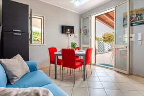 A modern living room with a blue sofa, a dining area with red chairs, a flat-screen TV, and a sliding glass door leading to an outdoor area. - Villa Tiffany with Private Terrace, Wi-Fi, Air Conditioning, and Garden View (Campofelice di Roccella)
