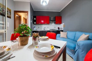 A compact living space with a dining area, kitchenette, and a blue sofa. - Villa Tiffany with Private Terrace, Wi-Fi, Air Conditioning, and Garden View (Campofelice di Roccella)