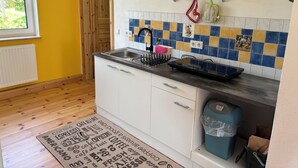 Una cocina con salpicadero de azulejos, un fregadero y una estufa. Hay una puerta de madera que conduce a otra habitación.