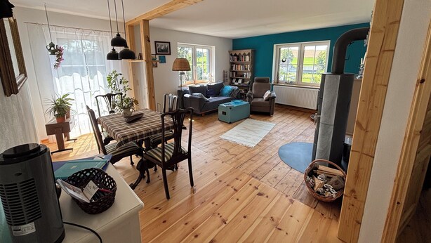 Amplia sala de estar con piso de madera, comedor con mesa y sillas, un sofá, una estantería y chimenea.