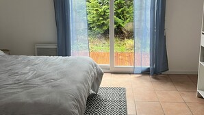 Une chambre avec un lit, un tapis à motifs, un radiateur et une vue sur la verdure, visible à travers une porte vitrée.