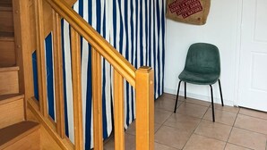 Un escalier en bois, un rideau à rayures et une chaise verte dans une pièce aux murs blancs et au sol carrelé.