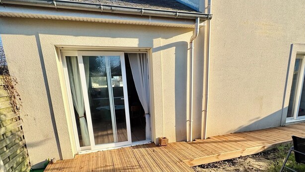 Une terrasse en bois avec une porte-fenêtre coulissante donnant sur un patio abrité.