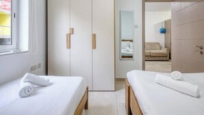 A hotel room with two beds, a wardrobe, a mirror, and a view of another room. - Live Where Malta Comes Alive, 2BR in Paceville! (St. Julian`s)