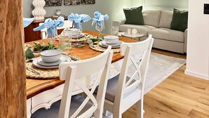 A dining area with a wooden table set for four, white chairs, a vase with greenery, and a wall-mounted light fixture. - Apartment "Fewo Sand 10 – Large" with Shared Terrace, Garden & Wi-Fi (Bamberg)