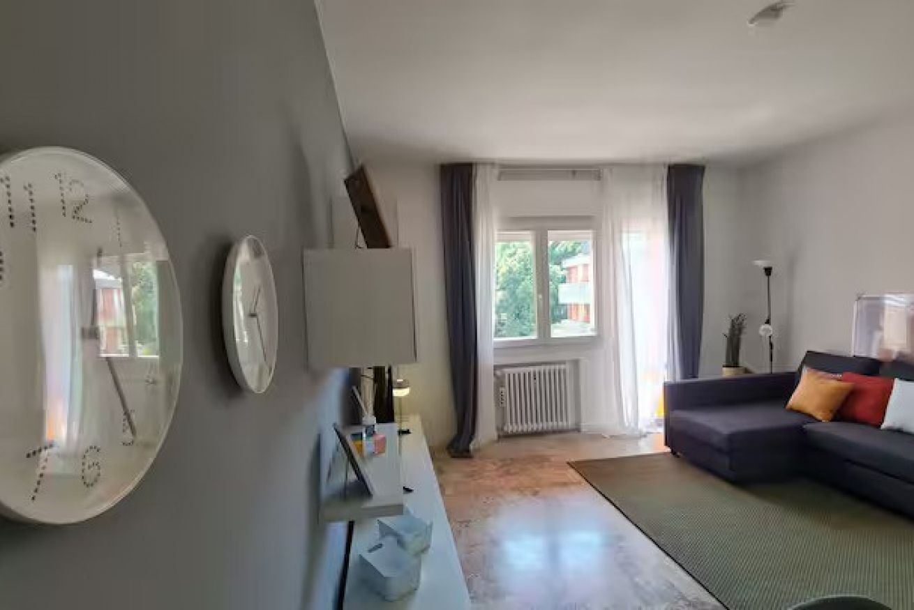 Ein modernes Wohnzimmer mit einer großen, runden Uhr, einer Couch und Blick ins Freie.