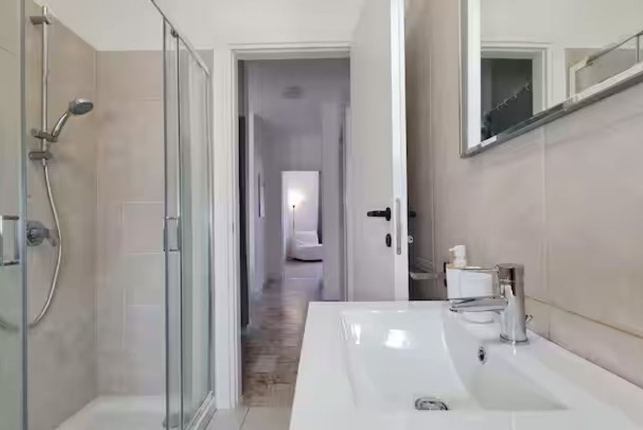 Un bagno moderno con cabina doccia in vetro, lavabo bianco e specchio.