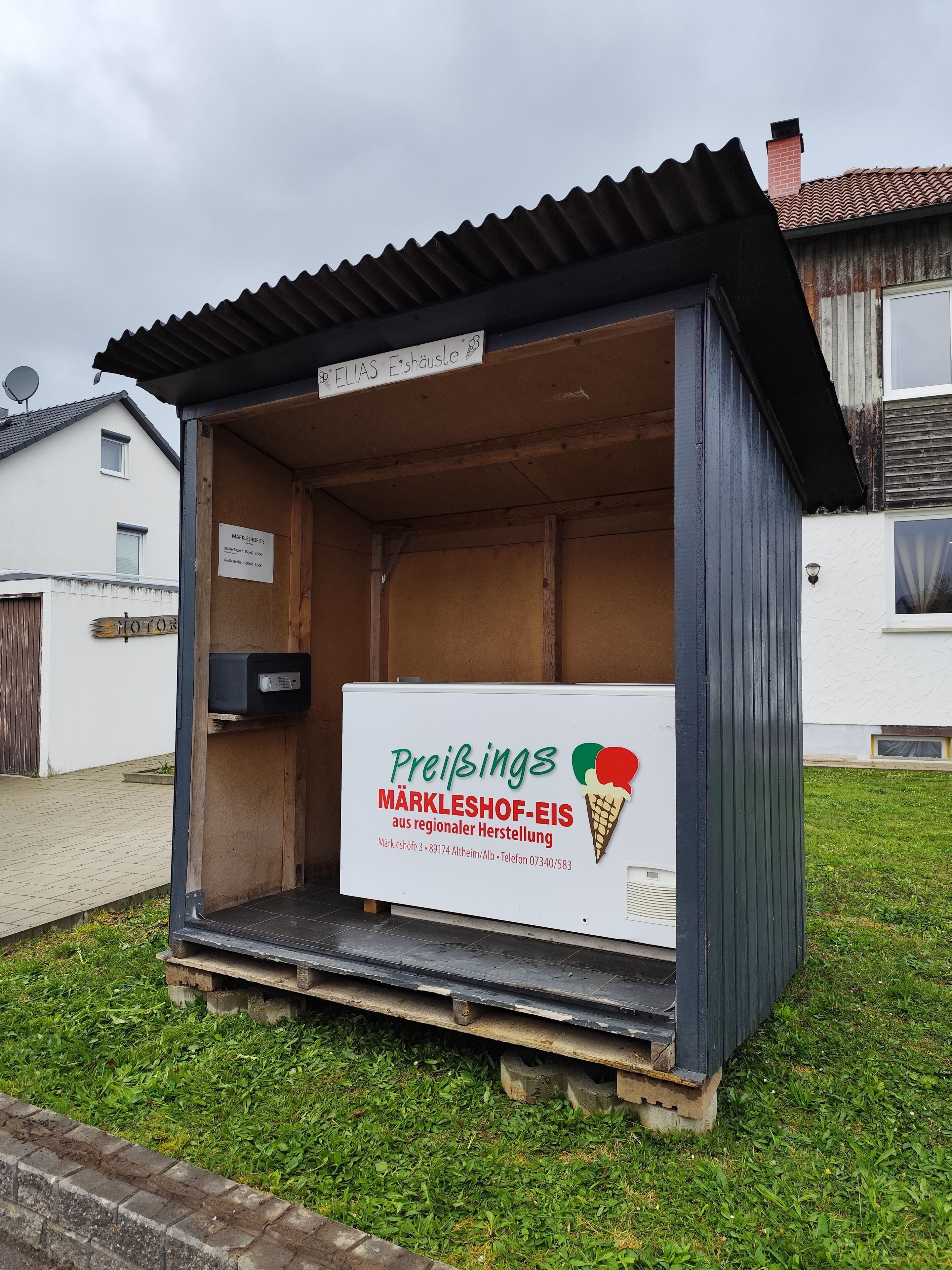 A small ice cream kiosk with a sign advertising 'Preibings Märkleshof-Eis' and contact information.