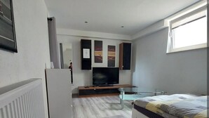 Quarto moderno com cama, televisão e uma pequena cozinha compacta.