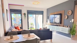 Uma sala de estar moderna com sofá, mesa de jantar, cadeiras, televisão e varanda com plantas.