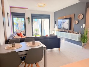 Un salon moderne comprenant un canapé, une table à manger, des chaises, un téléviseur et un balcon agrémenté de plantes.