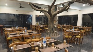 A restaurant with round tables and chairs, a large tree sculpture centerpiece, and a modern interior design. - JYOTI RESORT JOYPUR (Bishnupur)