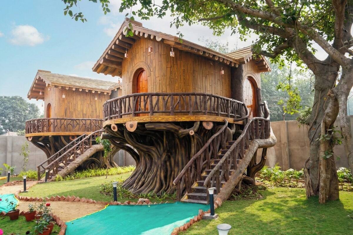 Una casa en árbol con fachada de madera, construida en el tronco de un árbol grande, que cuenta con un balcón y escaleras.