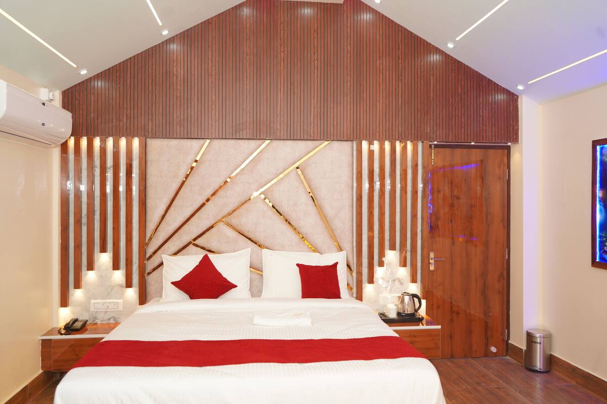 Un dormitorio moderno con cabecera de madera, una cama grande con ropa de cama blanca y almohadas rojas, mesitas de noche con lámparas y una puerta de madera.