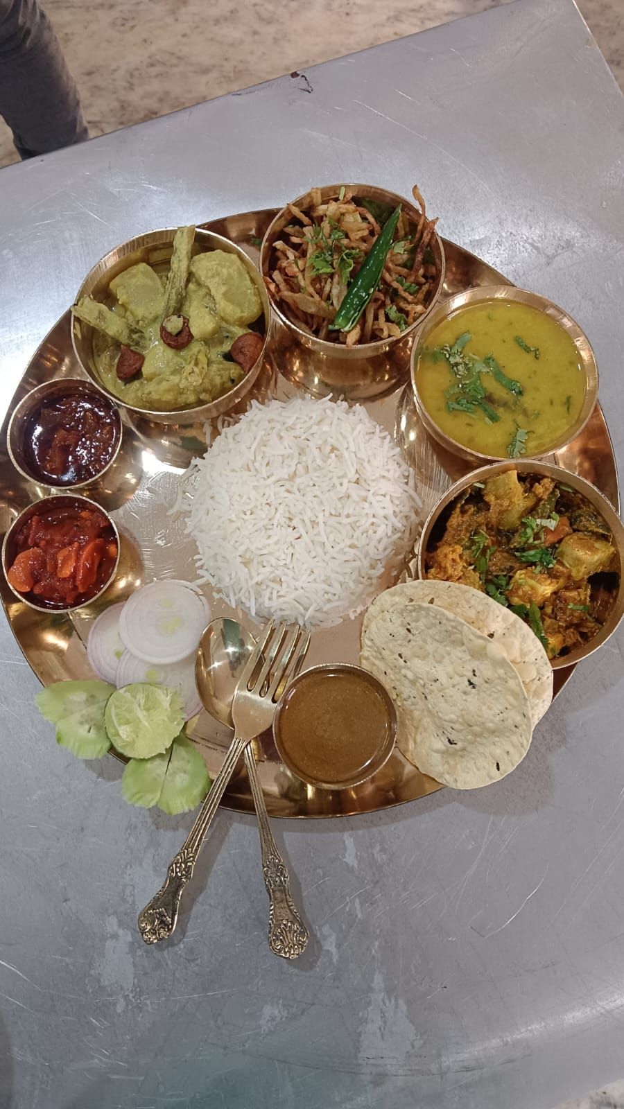 A traditional Indian meal served on a brass plate with rice, various curries, and a flatbread.