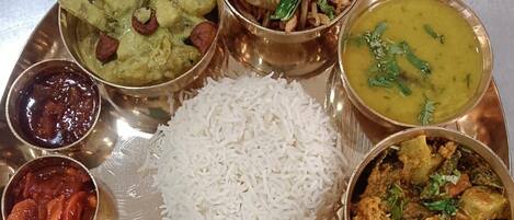 A traditional Indian meal served on a brass plate with rice, various curries, and a flatbread.