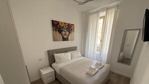 A bedroom with a bed, a nightstand, a painting, a window with curtains, and a mirror. - Delightful apartment recently renovated, central area well connected (Roma)