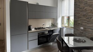 A modern kitchen with grey cabinets, a built-in oven, and a dining area with a glass table and chairs. - Delightful apartment recently renovated, central area well connected (Roma)