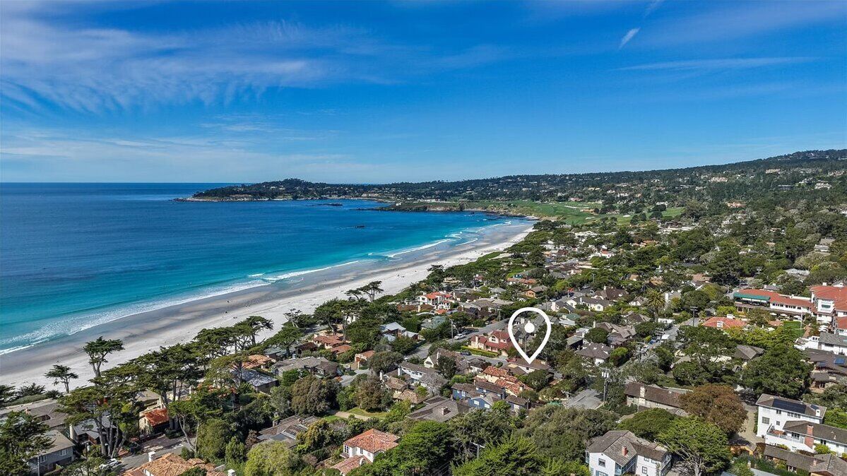 Una zona residencial a la costa amb cases, una platja i un paisatge amb turons al fons.