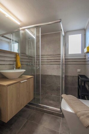 Une salle de bain moderne avec une douche à parois de verre, un meuble-lavabo en bois et un tapis de bain beige.