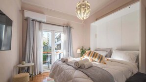 Une chambre avec un grand lit, un petit pouf rond, une table ronde et une vue sur l’extérieur.