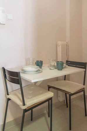 Un petit coin repas avec une table blanche et deux chaises, un bol, deux verres et une tasse bleue.