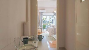 Un couloir étroit, avec une table à manger dressée pour deux personnes, qui mène à un balcon doté d’un lit et offrant une vue sur les immeubles.