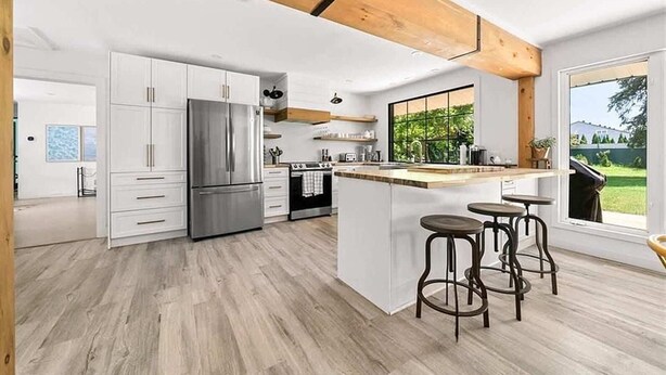 Una cocina moderna con armarios blancos, un refrigerador de acero inoxidable, un horno empotrado y un amplio ventanal con vistas al exterior.