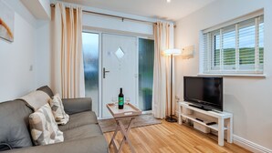 A modern living room with a sofa, a TV on a stand, and a door leading to a balcony.