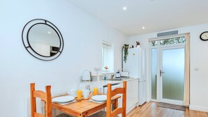 A modern kitchen with a dining area, white cabinets, a round mirror, and a wooden dining table with chairs.