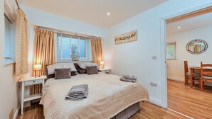 A bedroom with a large bed, bedside tables, a window with curtains, a wall-mounted artwork, and a wooden floor.