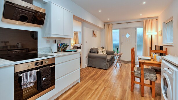 A compact kitchen with modern appliances, a dining area with a table and chairs, and a living space with a sofa.