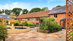 Ein Innenhof mit einem Brunnen, Backsteingebäuden und einer Holzpergola.
