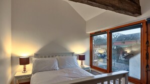 Ein Schlafzimmer mit einem Bett, zwei Nachttischen mit Lampen, einem Fenster mit Blick nach draußen und einem Holzbalken an der Decke.