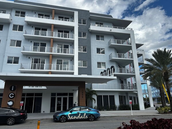Ein mehrstöckiges Hotel mit Balkonen, ein Auto vor der Fassade und eine Palme in der Nähe.